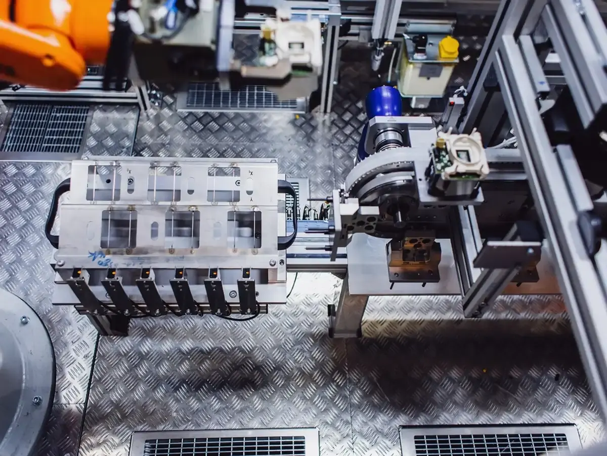Top-down view of an automated assembly cell with a workpiece carrier, sensors, and an industrial robot in production for custom machine building at AWM Arnstadt.