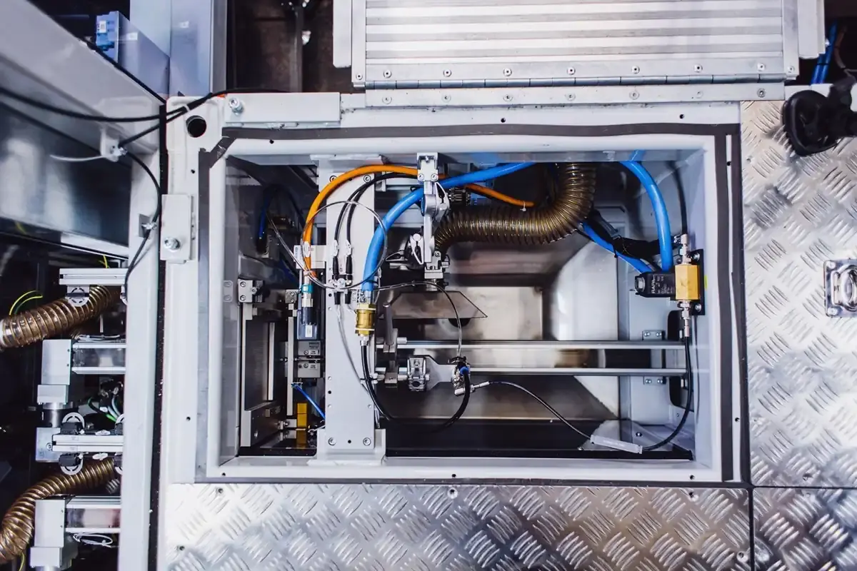 Detailed view of an enclosed process chamber with pneumatic controls, hose routing, and checker plate housing for quality-assured headlight assembly.