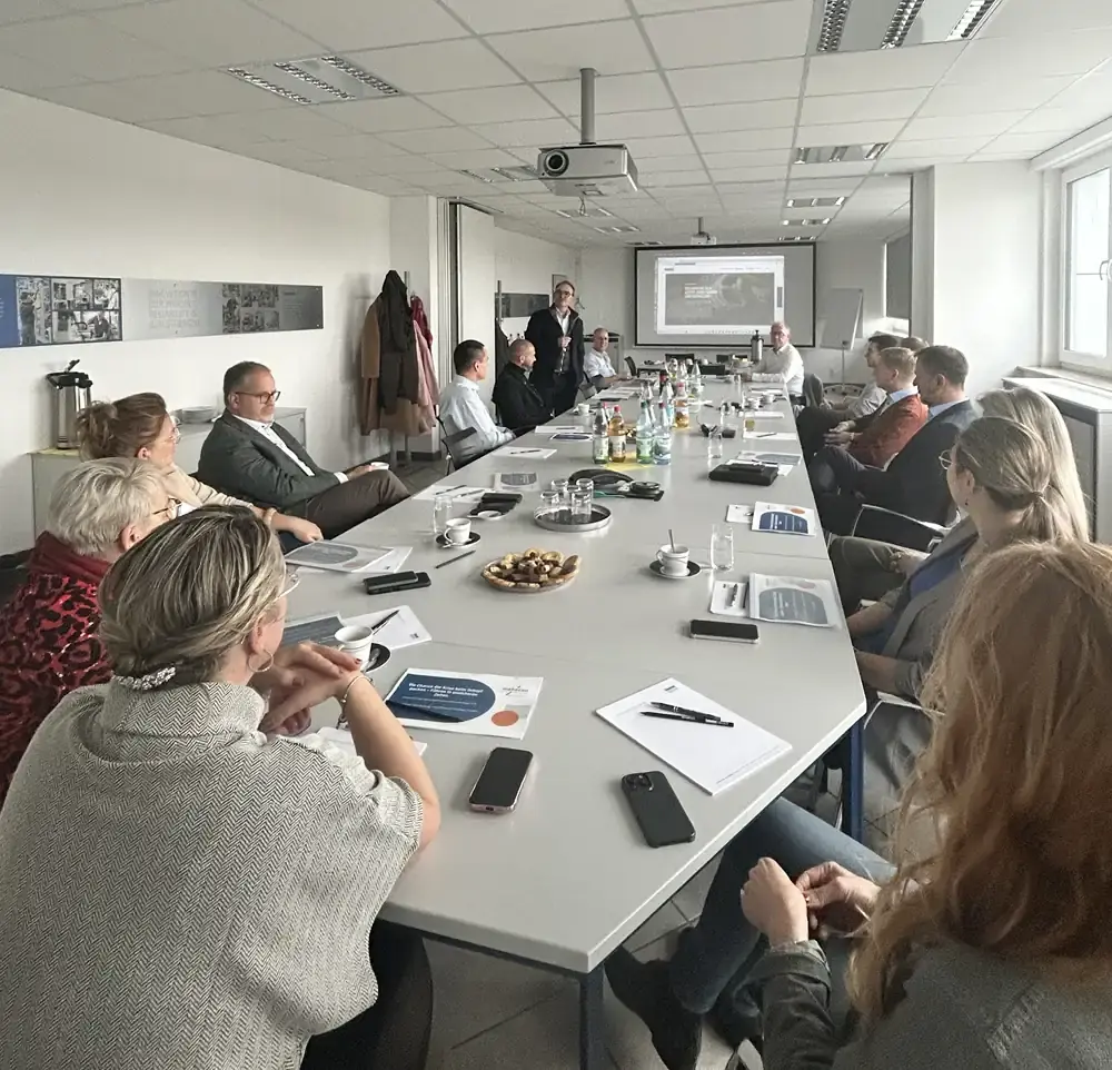 AWM team and managers gathered at a long conference table for a crisis strategy session featuring a projector presentation and meeting documents.