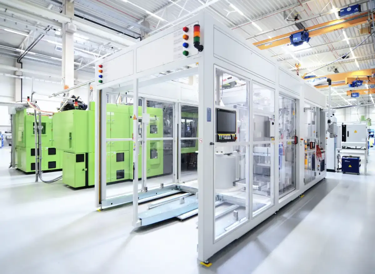 Highly automated AWM custom machine with signal tower and glass safety panels alongside other industrial equipment in a clean production environment.