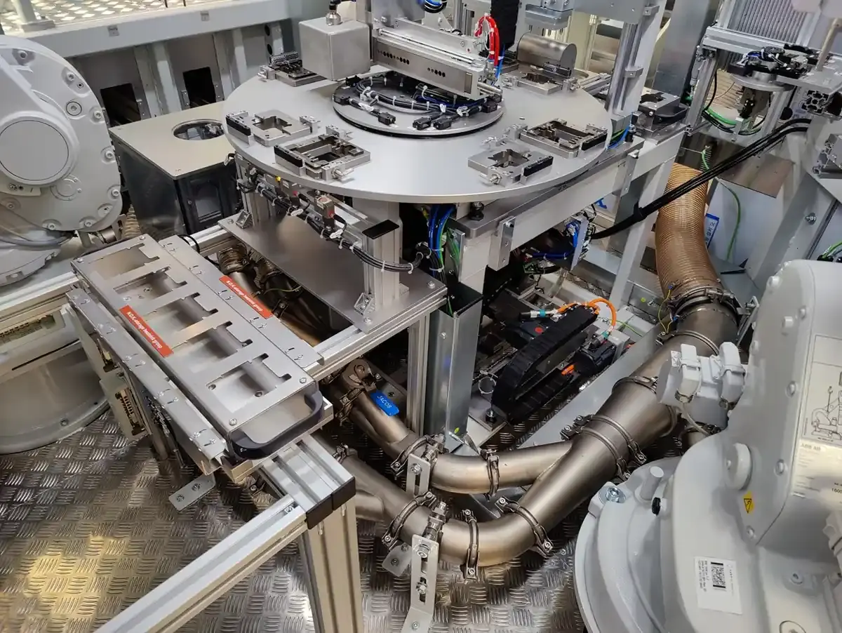View of an automated rotary indexing table with integrated extraction pipes, pneumatic lines, and robot-assisted handling stations in custom machine building at AWM Arnstadt.