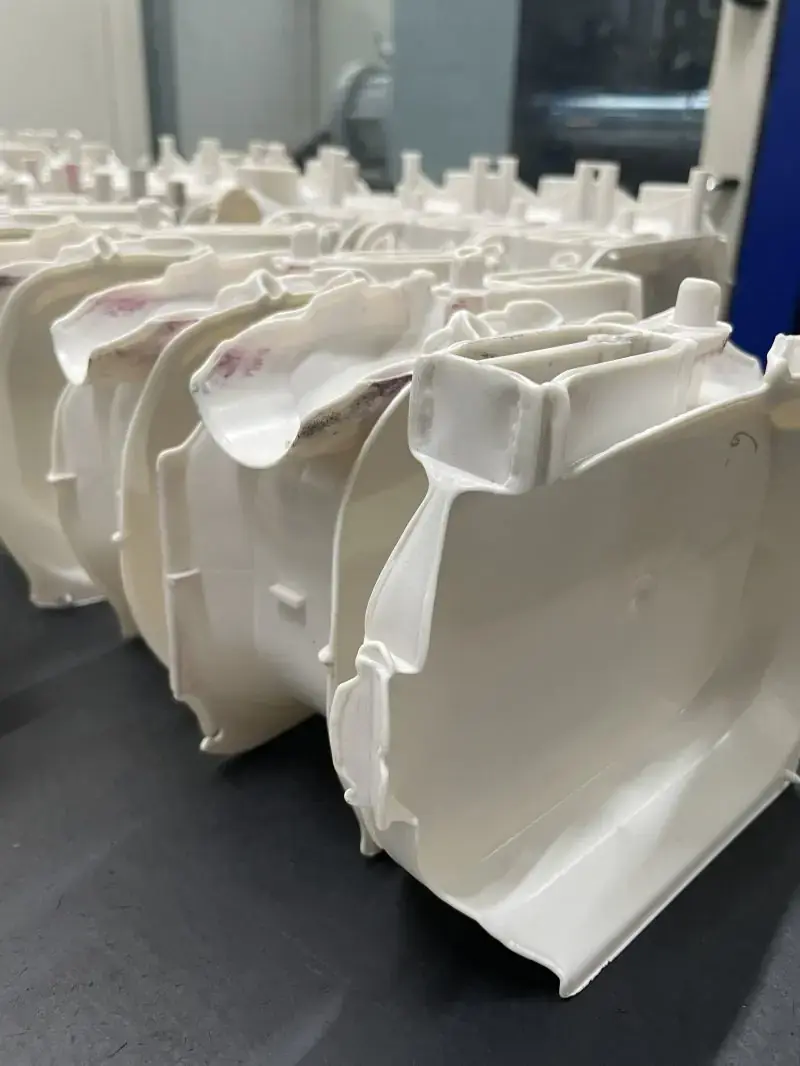 Row of manufactured white plastic components arranged on a surface in an industrial production environment.