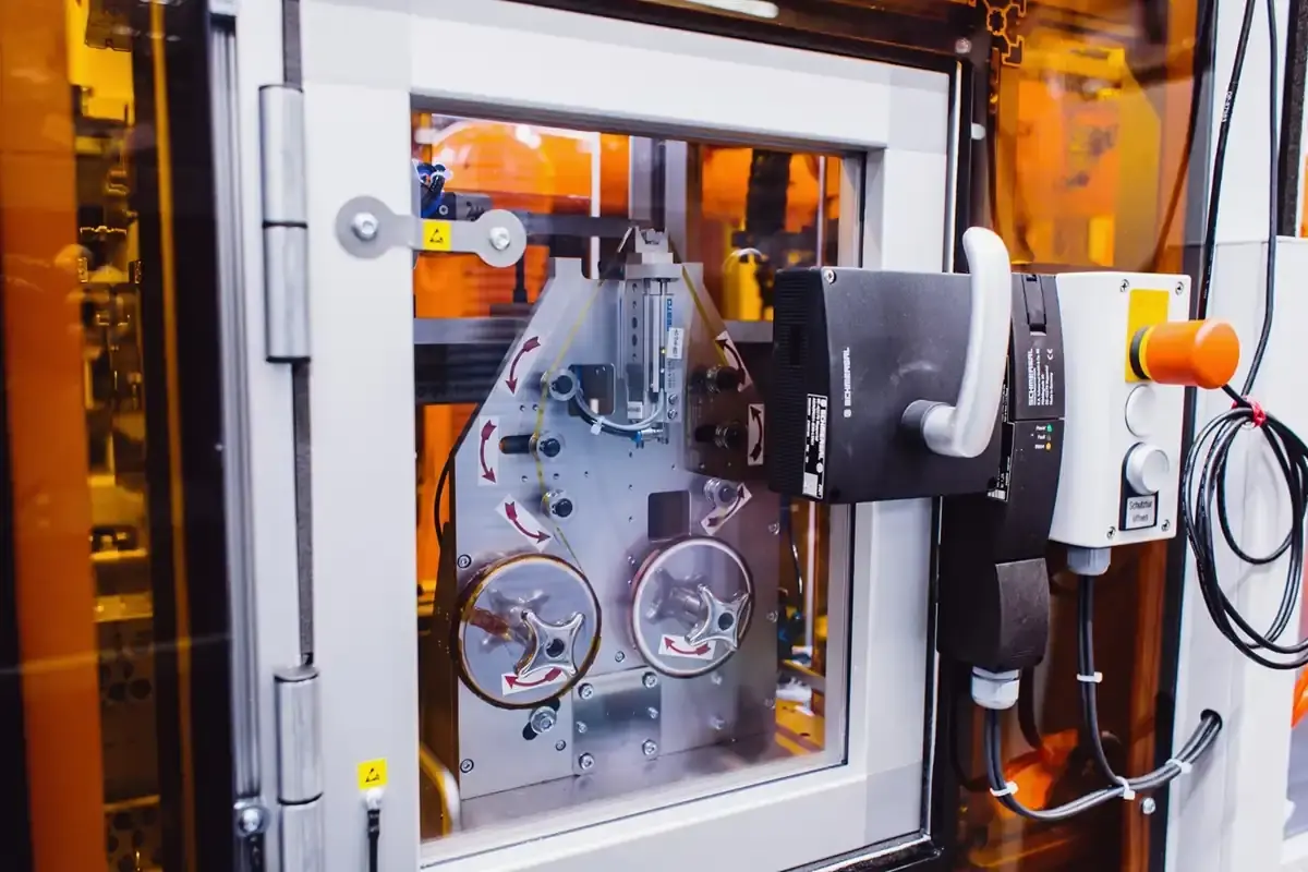 Automated reel-to-reel material feeding system with guide rollers, Schmersal safety switch, and transparent access door in AWM Arnstadt custom machine construction.