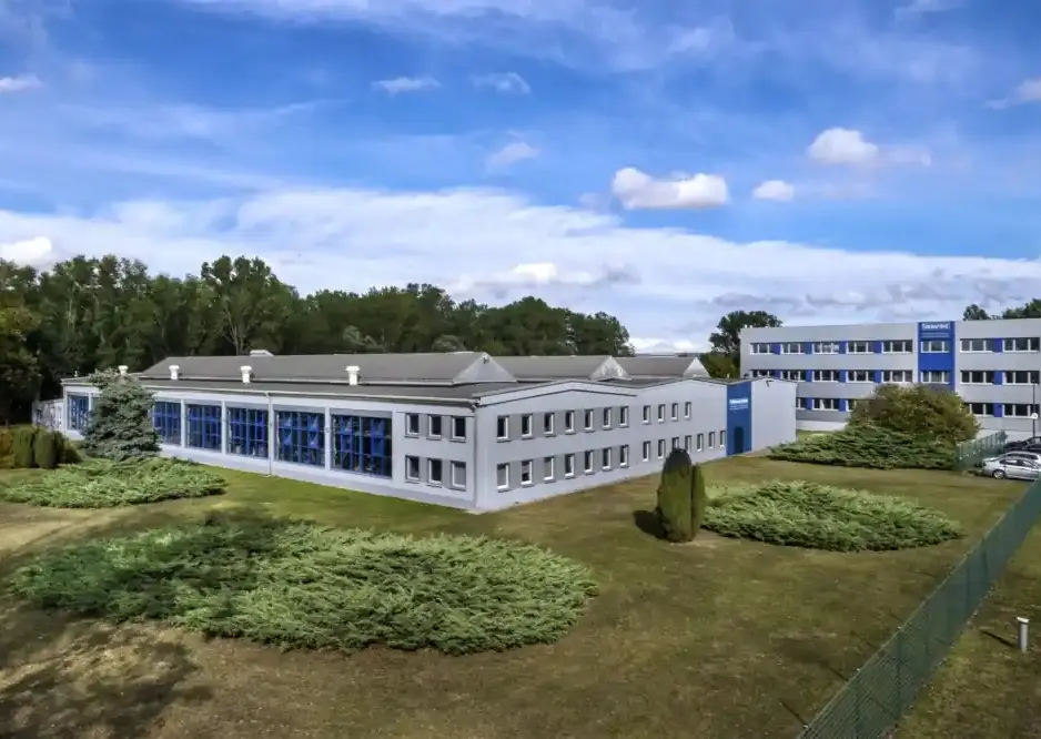 Exterior view of the Arnstädter Werkzeug- und Maschinenbau GmbH company premises, showing the production hall, office building, and landscaped green area under a blue sky.