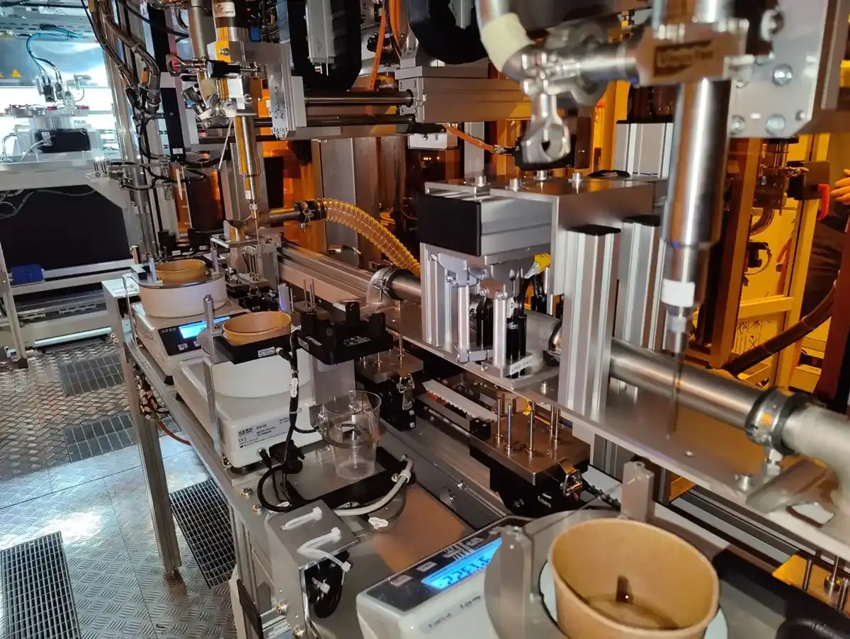 View of an automated assembly line with dispensing units, measuring cells, and pneumatic components from Arnstädter Werkzeug- und Maschinenbau GmbH.