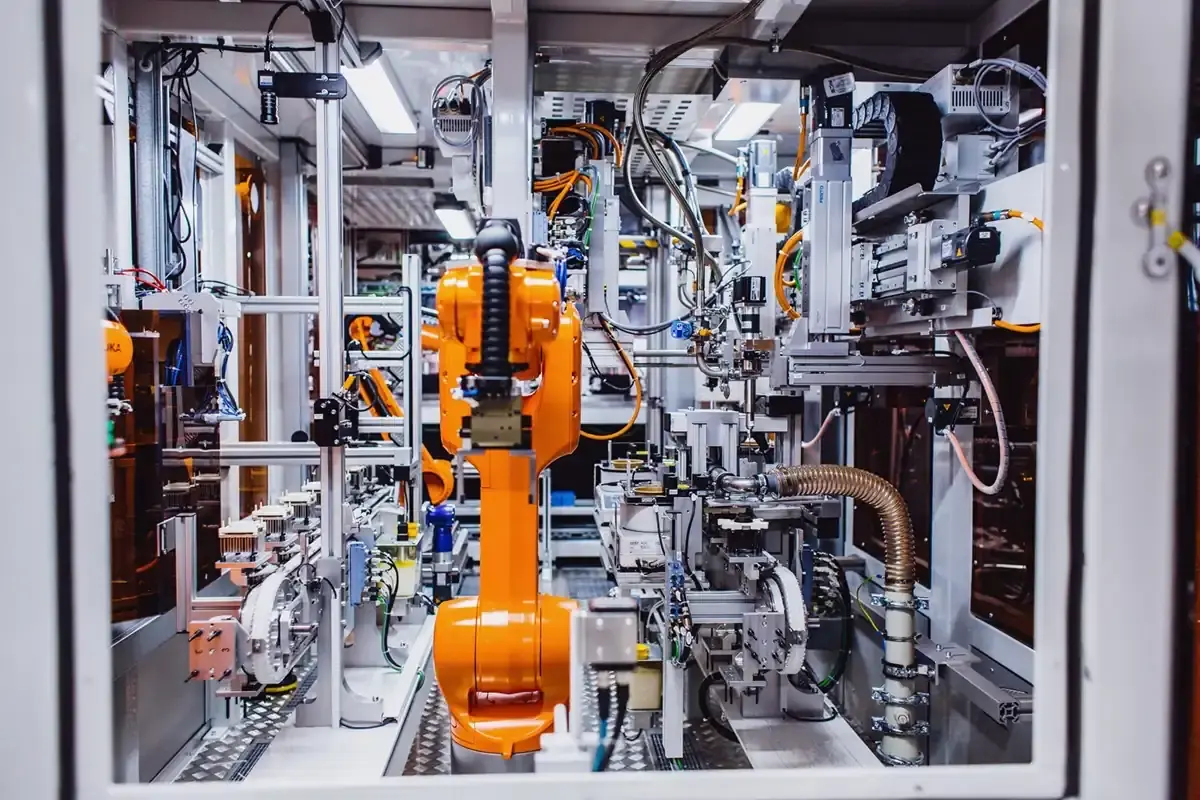 Interior view of a fully automated AWM assembly cell featuring an orange KUKA industrial robot, linear axes, and interconnected conveyor technology.