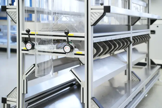 Close-up of the lower section of a separation station made of aluminum profiles featuring a transparent drop tube, rotary knobs, and metallic guide plates.